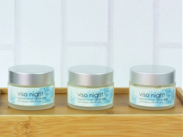 Viso night facial moisturiser in glass pots with silver lids on wood with white brick background